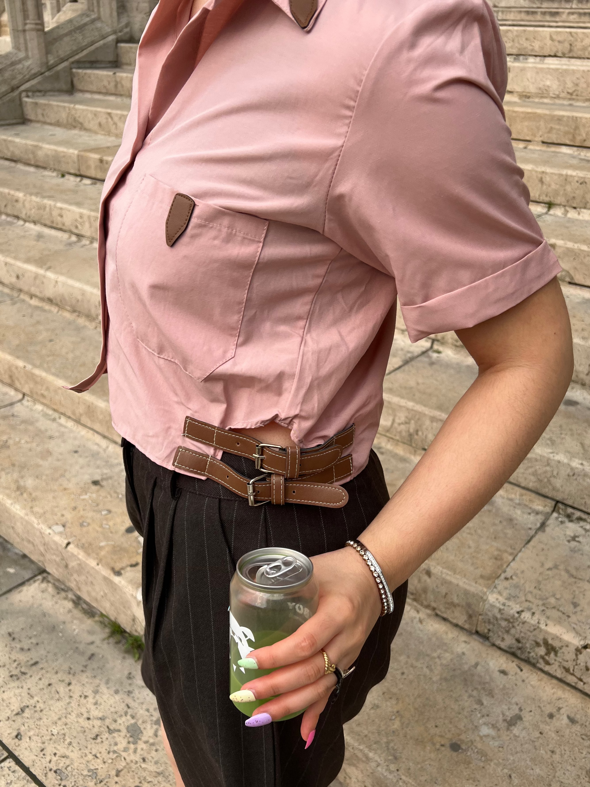Person wearing a pink shirt and dark pants, holding a can, standing on stone steps.
